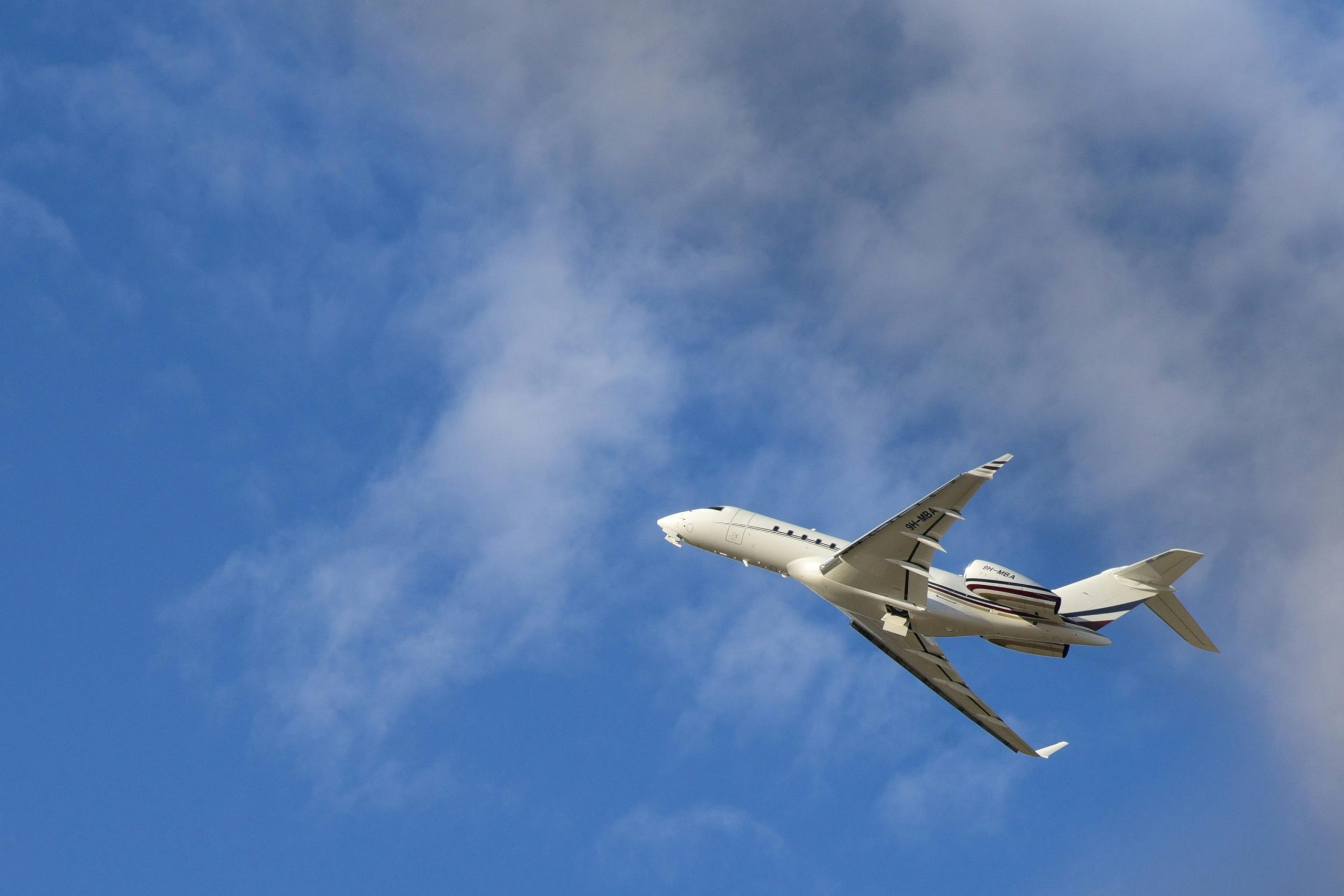 Commercial jet airplane flying high with a clear blue sky and clouds in the backdrop.